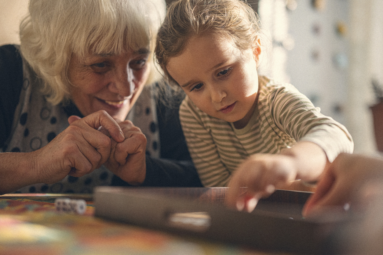 A senior woman playing a board game with a young girl.