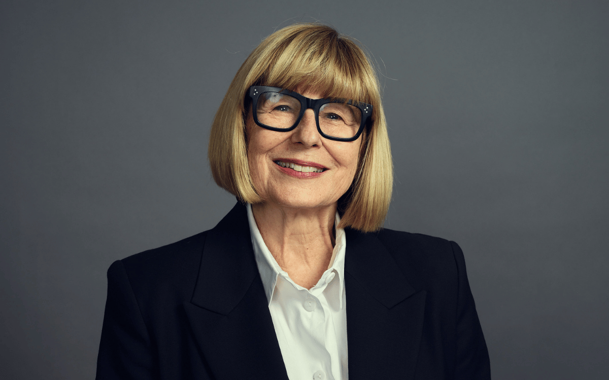 A headshot of Fair Work Ombudsman Anna Booth wearing a black blazer and white shirt on a grey background.